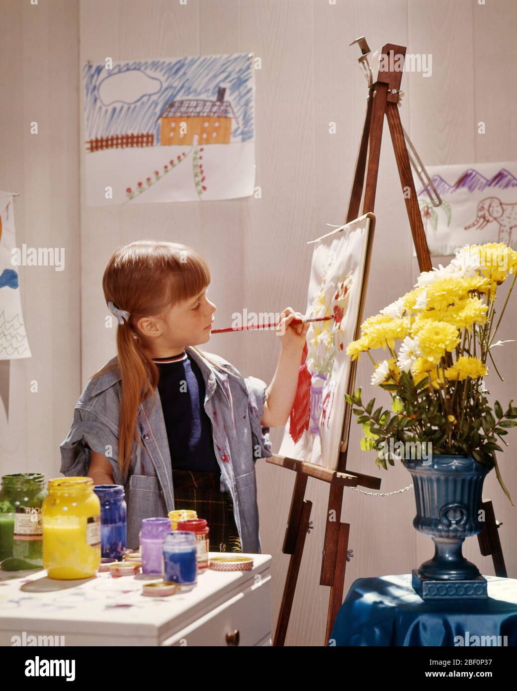 1980s GIRL AT EASEL PAINTING DRAWING PAINTS CANVAS ART ARTIST PONYTAIL SMOCK YELLOW CHRYSANTHEMUM FLOWERS IN VASE  - kj9587 PHT001 HARS CANVAS HAIRSTYLE CHRYSANTHEMUM CREATOR OCCUPATIONS PONYTAIL PRIMARY ART CLASS CONCEPTUAL IMAGINATION PAINTS SMOCK COOPERATION CREATE CREATIVITY GRADE SCHOOL GROWTH PIG TAIL BANGS CAUCASIAN ETHNICITY OLD FASHIONED Stock Photo