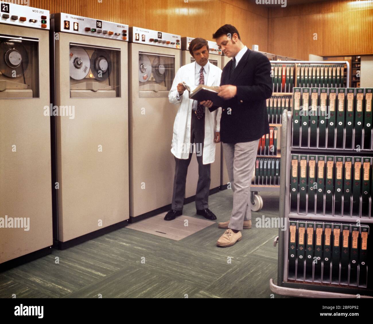 1980s TWO ANONYMOUS MEN MANAGER AND TECHNICIAN STANDING TOGETHER CHECKING A MANUAL BESIDE COMPUTER MAINFRAME TAPE STORAGE SILOS - ko1761 PHT001 HARS INFORMATION STORAGE REVOLUTION CHECKING LIFESTYLE HISTORY JOBS MANAGER COPY SPACE FULL-LENGTH PERSONS TECHNICIAN MALES EXECUTIVES DATA SUCCESS SKILL OCCUPATION SKILLS MAINFRAME MANUAL AND NETWORKING KNOWLEDGE LEADERSHIP PROGRESS INNOVATION A AUTHORITY OCCUPATIONS SILOS HIGH TECH BOSSES CONCEPTUAL BESIDE SUPPORT FACILITY ANONYMOUS COOPERATION IDEAS MANAGERS MID-ADULT MID-ADULT MAN PRECISION REEL TO REEL SOLUTIONS TECHNICAL CAUCASIAN ETHNICITY Stock Photo