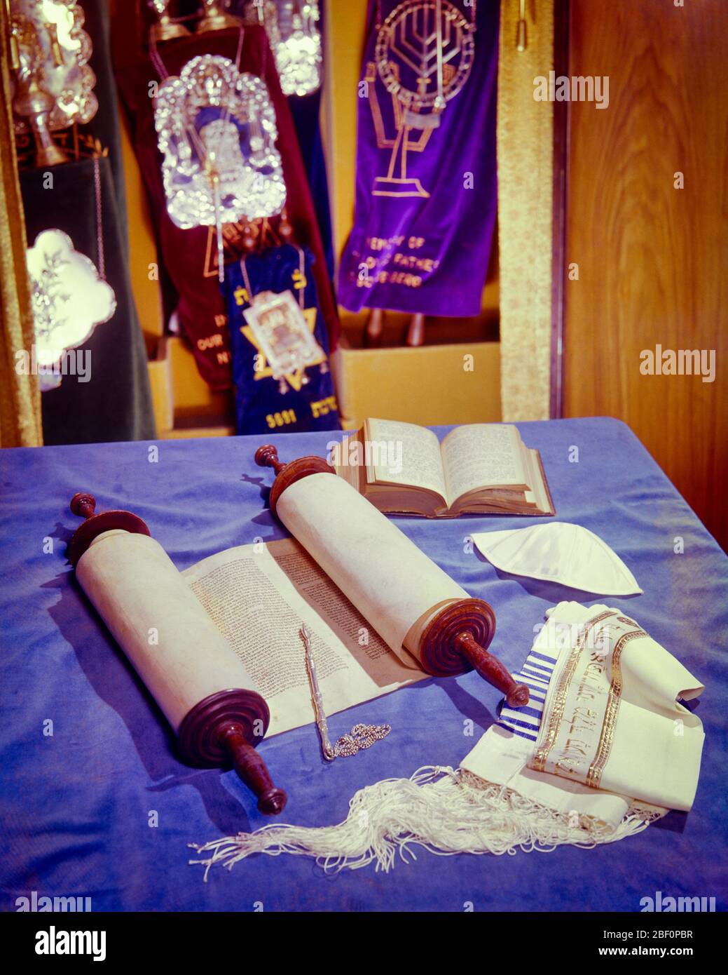 1970s OPEN TORAH WITH YAD PRAYER SHAWL TALLIT WHITE KIPPAH AND OPEN ARK OF THE LAW  HOLDS OTHER TORAHS IN BACKGROUND - kr29445 PHT001 HARS TORAH Stock Photo