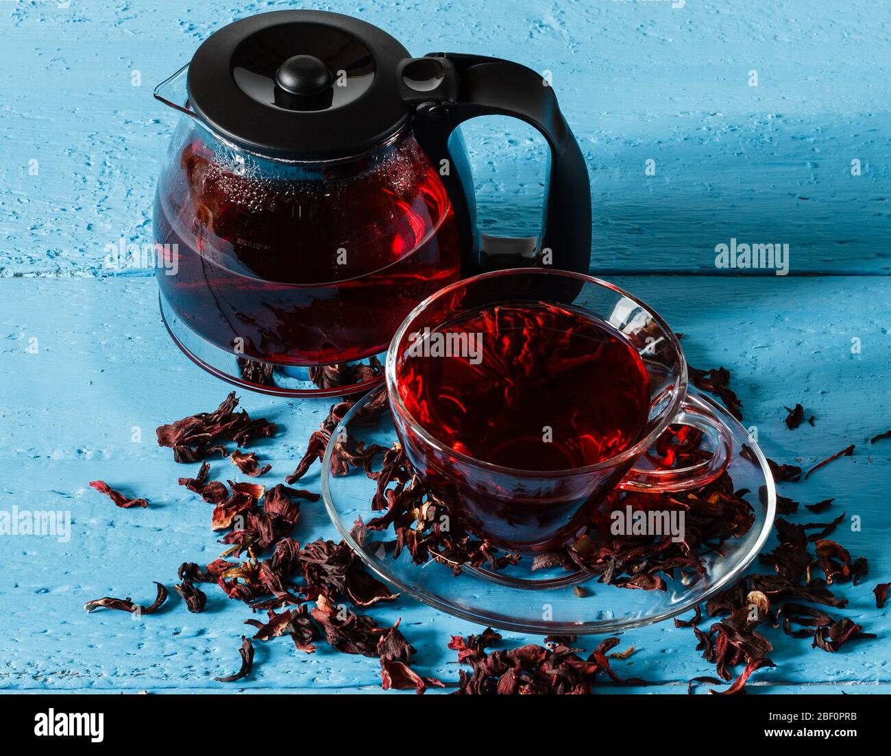 Cup of Karkadeh Red Tea and kettle with Dry Flowers on a blue wooden ...