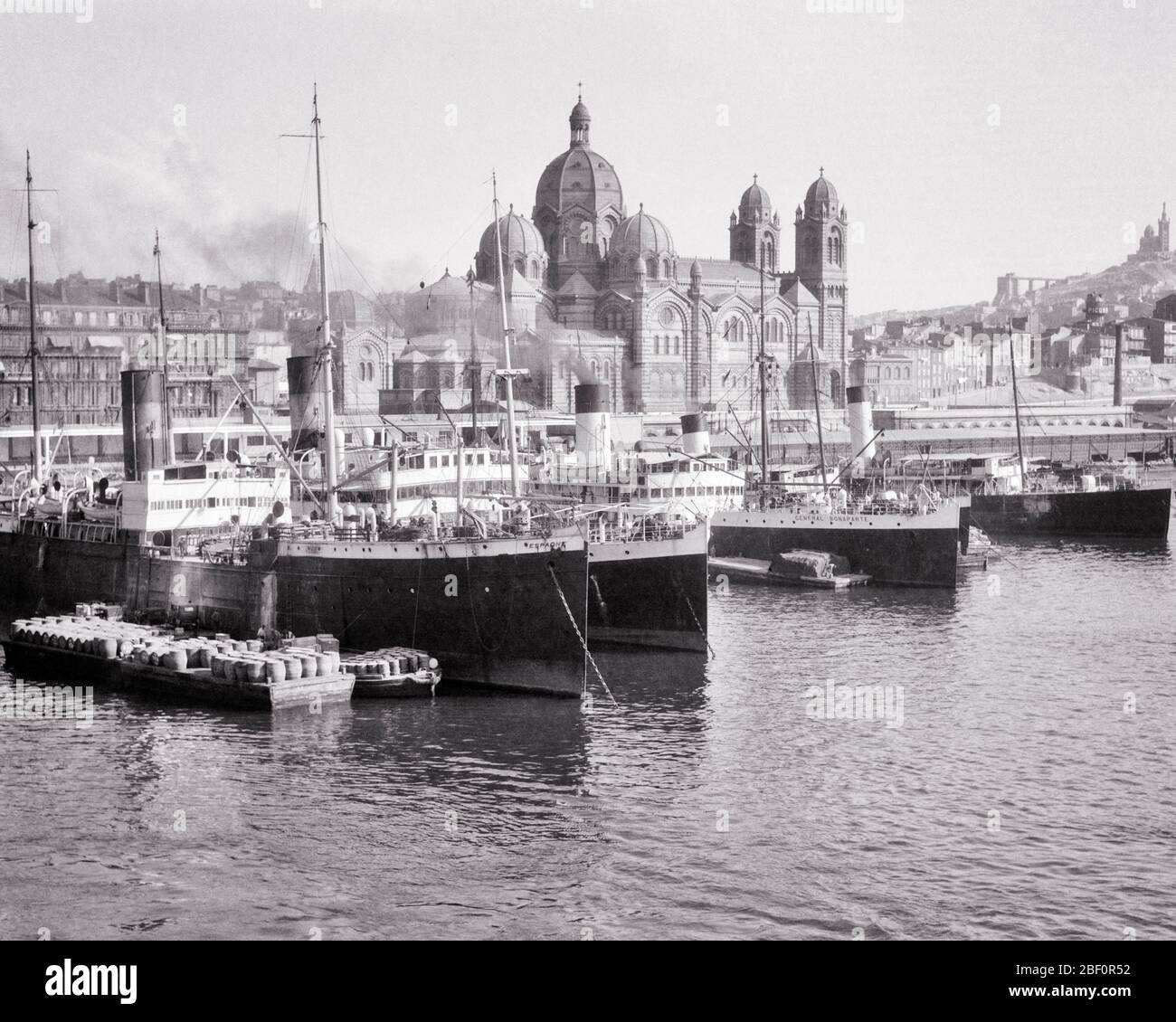 1920s CARGO SHIPS DOCKED IN OLD PORT THE CATHEDRAL AND BASILICA NOTRE-DAME DE LA GARDE BEYOND ON HILLTOP MARSEILLE FRANCE - r2974 HAR001 HARS DOCKED ROMANESQUE CITIES FREIGHTER MARSEILLES COMMERCE GARDE HILLTOP SHIPPING STEAM SHIPS BASILICA BLACK AND WHITE HAR001 LA NOTRE-DAME OLD FASHIONED VESSEL Stock Photo