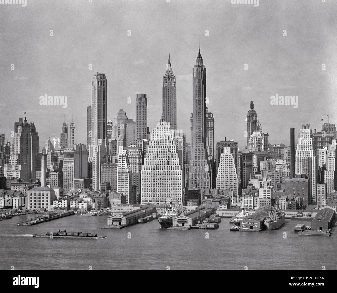 1940s SKYLINE OF DOWNTOWN FINANCIAL DISTRICT NYC SPIRES OF WOOLWORTH BUILDING IRVING TRUST AND 40 WALL STREET FROM BROOKLYN - r4127 HAR001 HARS WOOLWORTH NYC REAL ESTATE CONCEPTUAL NEW YORK STRUCTURES CITIES EDIFICE NEW YORK CITY PANORAMIC WATERFRONT BLACK AND WHITE DISTRICT EAST RIVER HAR001 IRVING OLD FASHIONED PIERS SKYLINES SKYSCRAPERS SPIRES Stock Photo