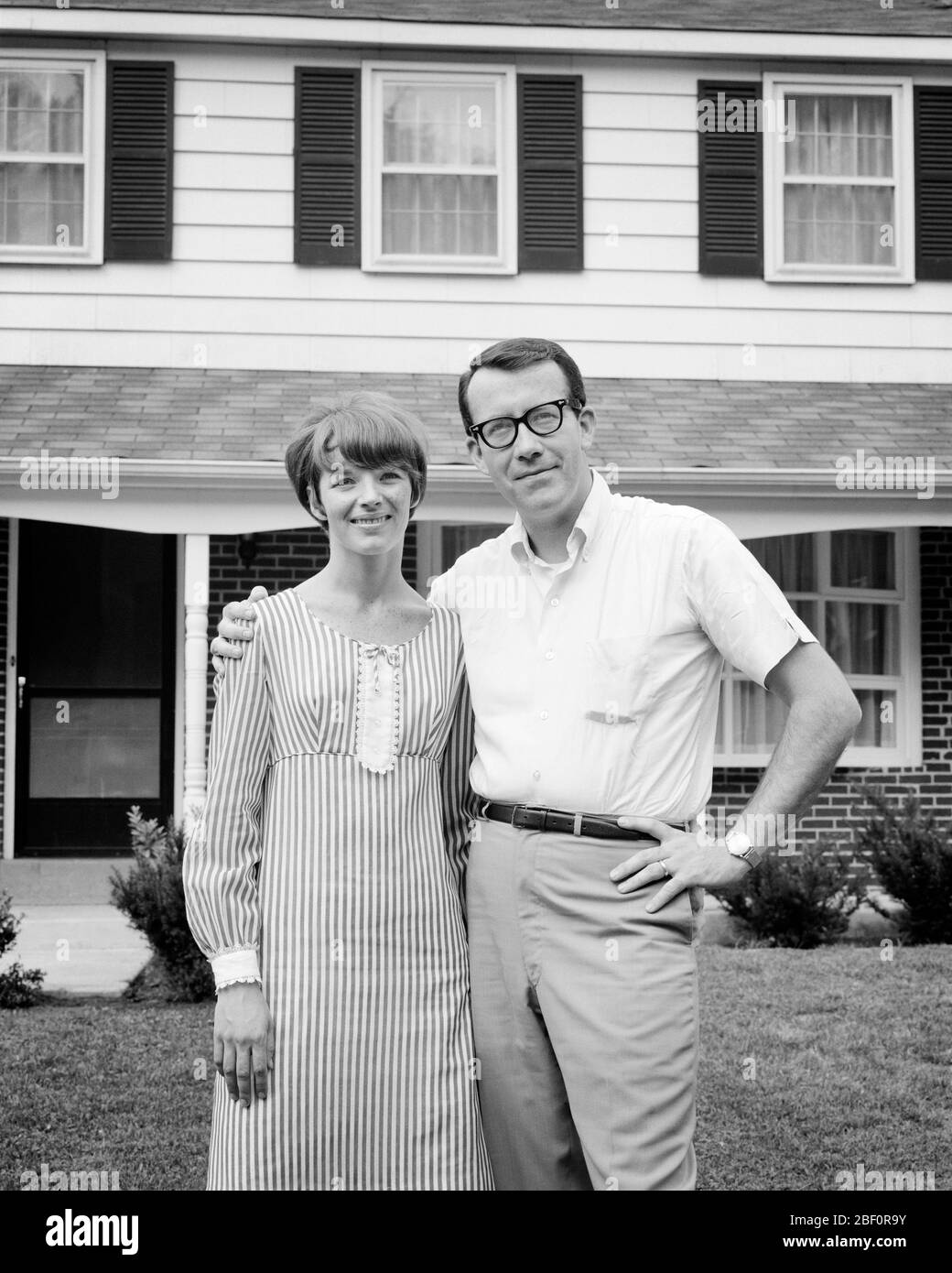 1960s COUPLE STANDING IN FRONT OF THEIR HOME MAN HAS ARM AROUND WIFE’S SHOULDERS WOMAN WEARING STRIPED DRESS - s15491 HAR001 HARS LIFESTYLE SATISFACTION FEMALES HOUSES STRIPED MARRIED SPOUSE HUSBANDS HOME LIFE COPY SPACE FRIENDSHIP HALF-LENGTH LADIES PERSONS RESIDENTIAL MALES BUILDINGS CONFIDENCE B&W PARTNER EYE CONTACT DREAMS HAPPINESS CHEERFUL EXTERIOR PRIDE HOMES SMILES CONNECTION JOYFUL RESIDENCE STYLISH IN FRONT OF DREAM HOUSE COOPERATION MID-ADULT MID-ADULT MAN MID-ADULT WOMAN TOGETHERNESS WIVES YOUNG ADULT MAN YOUNG ADULT WOMAN BLACK AND WHITE CAUCASIAN ETHNICITY HAR001 OLD FASHIONED Stock Photo