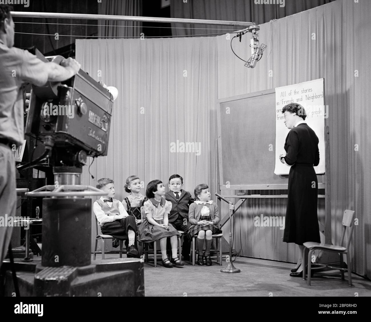 1950s MAN OPERATING TELEVISION CAMERA SHOWING WOMAN TEACHER INSTRUCTING READING CLASS FOR FIRST THROUGH THIRD GRADE STUDENTS - s3734 HAR001 HARS FIRST COMMUNITY URBAN OLD TIME NOSTALGIA MEDIA OLD FASHION 1 THROUGH JUVENILE COMMUNICATION TECHNOLOGY TEAMWORK LIFESTYLE FIVE FEMALES 5 JOBS SHOWING COPY SPACE FULL-LENGTH LADIES PERSONS CARING MALES ENTERTAINMENT B&W TELEVISIONS PERFORMING ARTS WIDE ANGLE SKILL GRADE OCCUPATION SKILLS OPERATING BROADCASTING DISCOVERY CUSTOMER SERVICE KNOWLEDGE PROGRESS EDUCATIONAL OPPORTUNITY AUTHORITY OCCUPATIONS THIRD INSTRUCTING HIGH TECH CONNECTION CONCEPTUAL Stock Photo