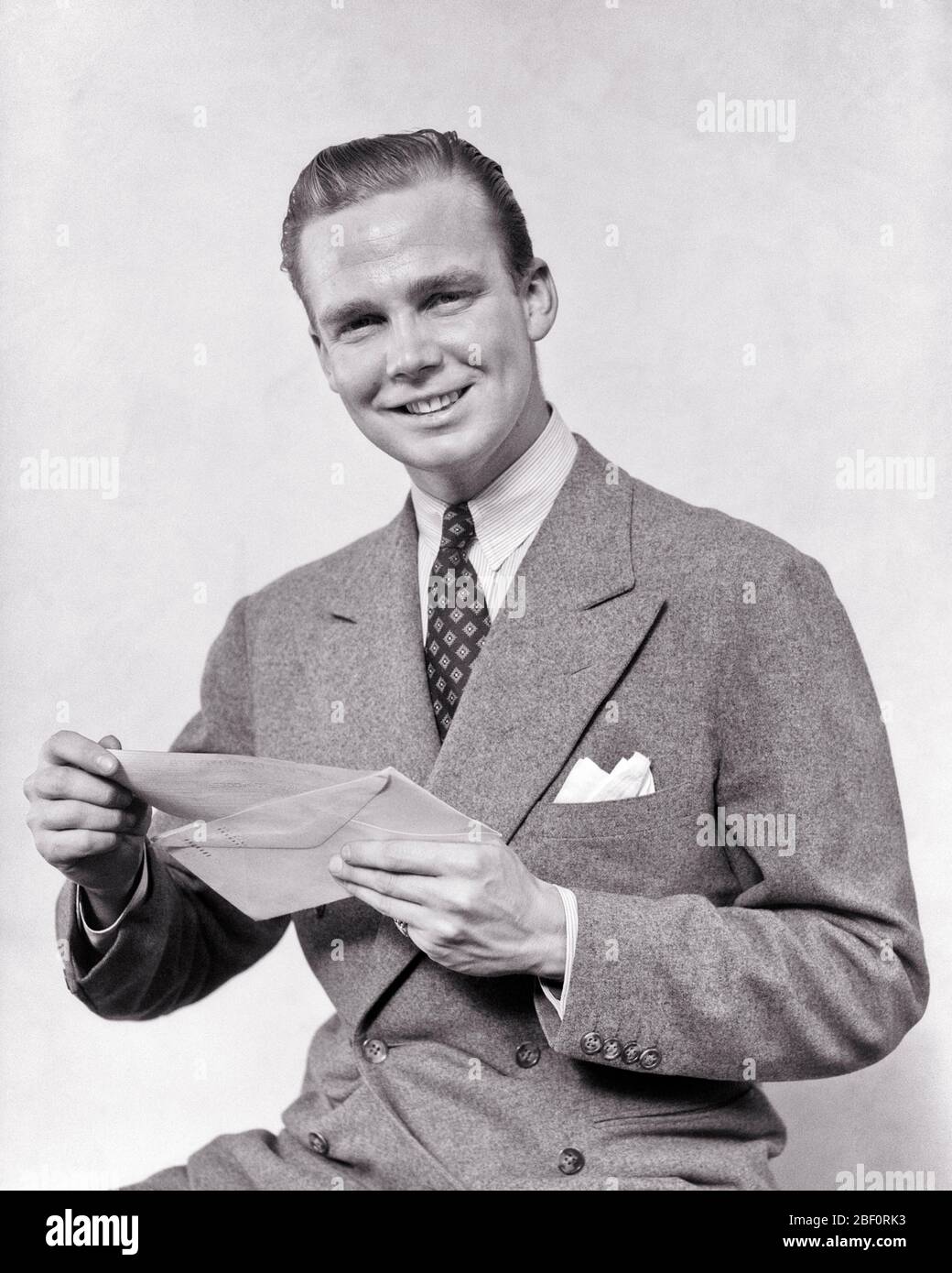 1930s SMILING MAN HOLDING CHECK LETTER AND OPEN ENVELOPE WEARING DOUBLE BREASTED SUIT LOOKING AT CAMERA - s8182 HAR001 HARS JOY LIFESTYLE SATISFACTION STUDIO SHOT HEALTHINESS COPY SPACE HALF-LENGTH PERSONS MALES B&W EYE CONTACT SUIT AND TIE HAPPINESS CHEERFUL CUSTOMER SERVICE AND GOOD NEWS OCCUPATIONS PAYMENT SMILES UPSCALE AFFLUENT JOYFUL STYLISH BREASTED WELL-TO-DO YOUNG ADULT MAN BLACK AND WHITE CAUCASIAN ETHNICITY HAR001 OLD FASHIONED Stock Photo