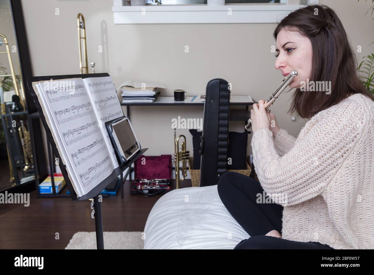 An attractive young brunette caucasian woman working from home by teaching music via video call during the Covid 19 crisis. Stock Photo