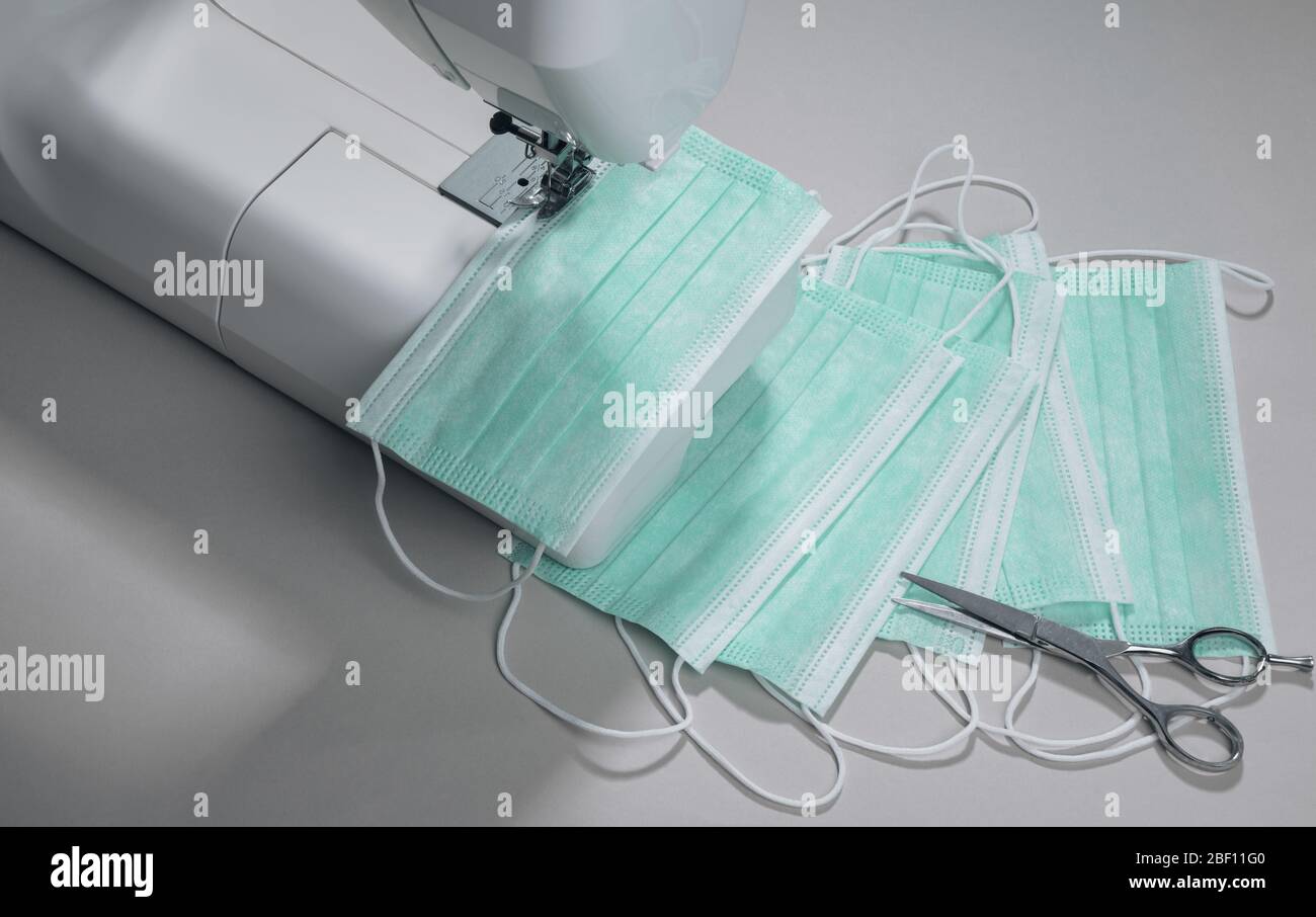 Surgical masks manufacturing process. Top view of Sewing machine and pile of medical masks and scissors on gray Stock Photo