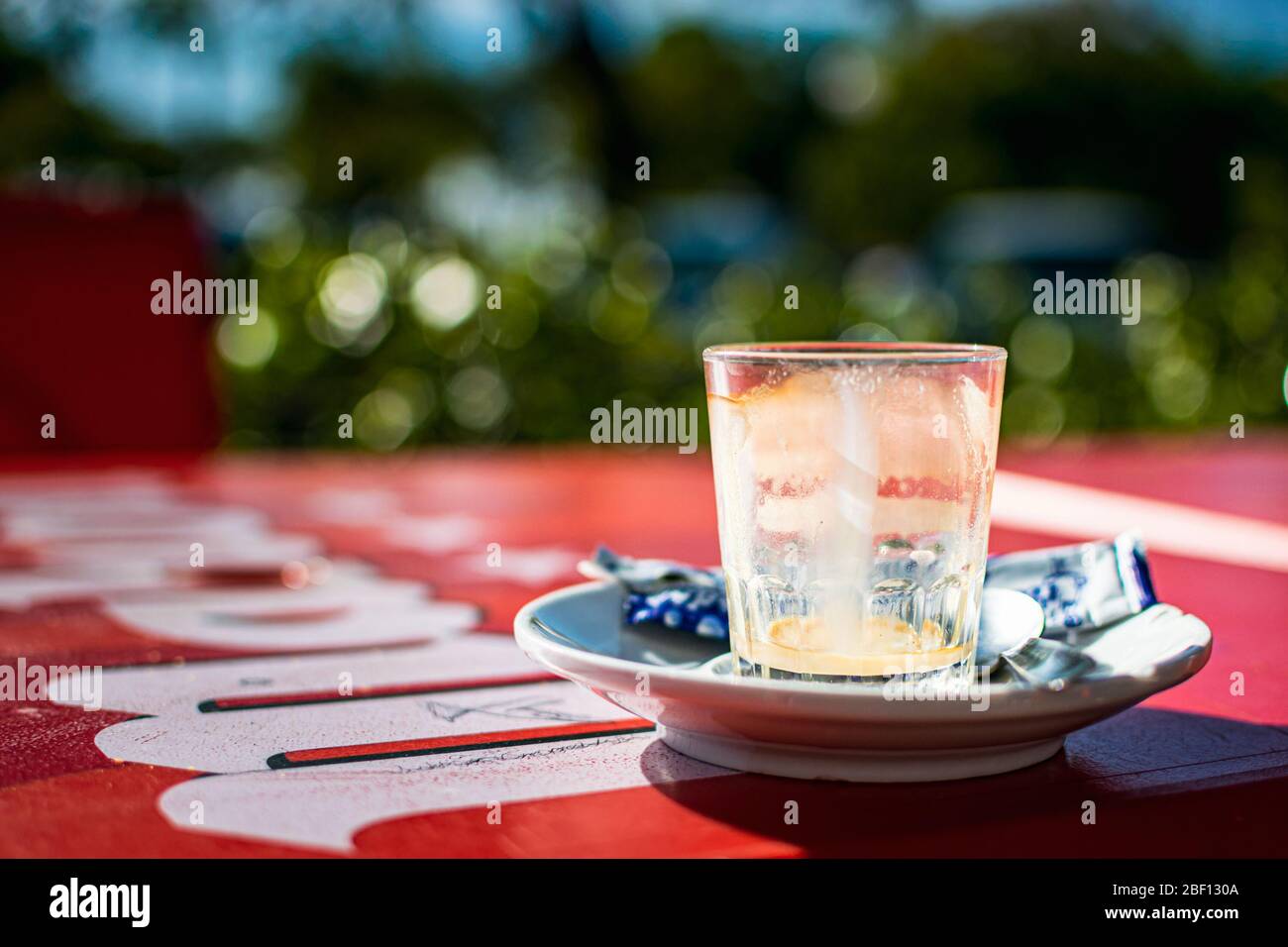 An empty glass after a 'bombon' (typical coffee drink in the region) on a red outdoor terrace table. Stock Photo