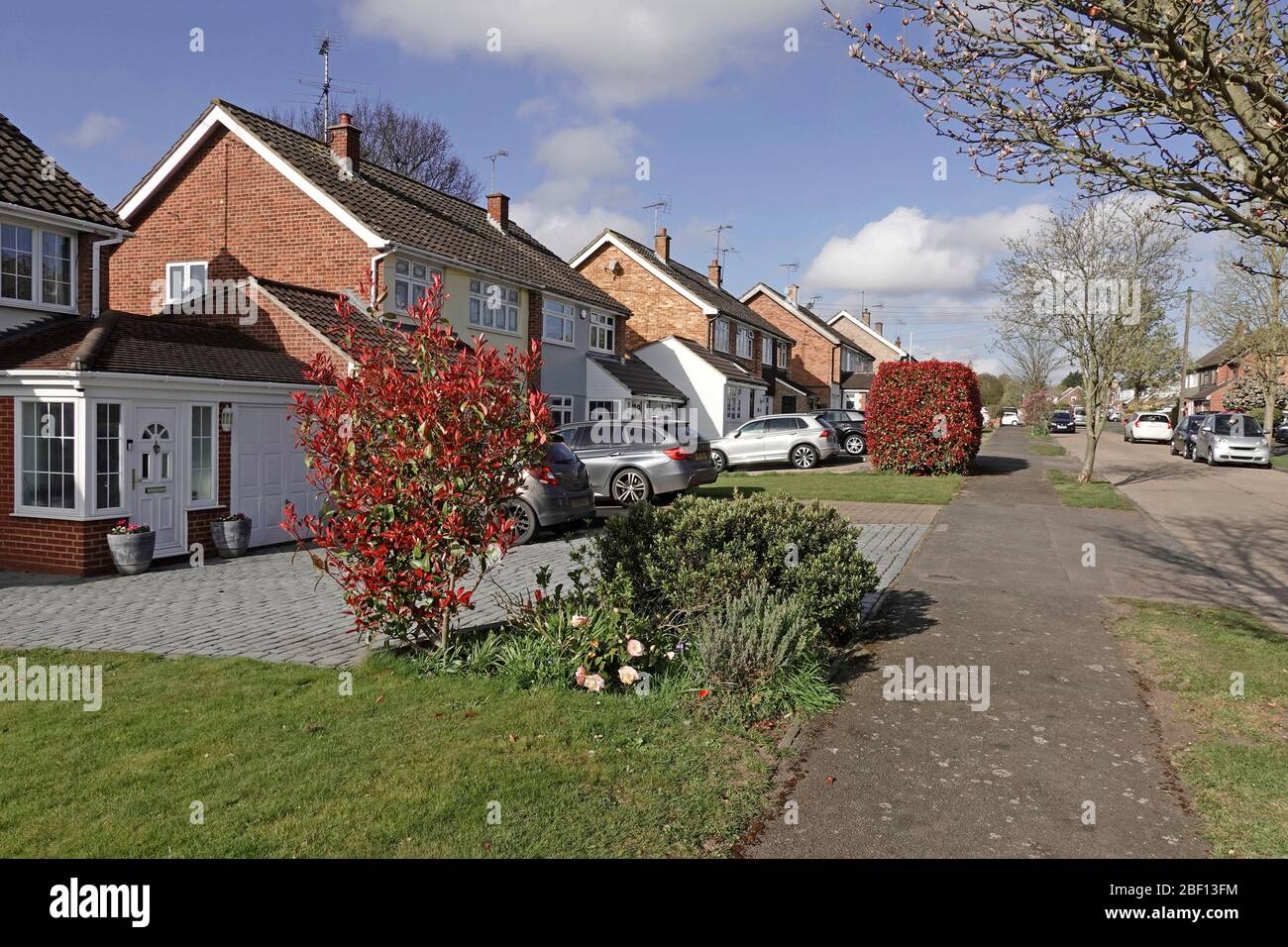 Housing street scene some semi detached homes paving over front garden with paved driveway for car parking space some keep home lawn  Essex England UK Stock Photo