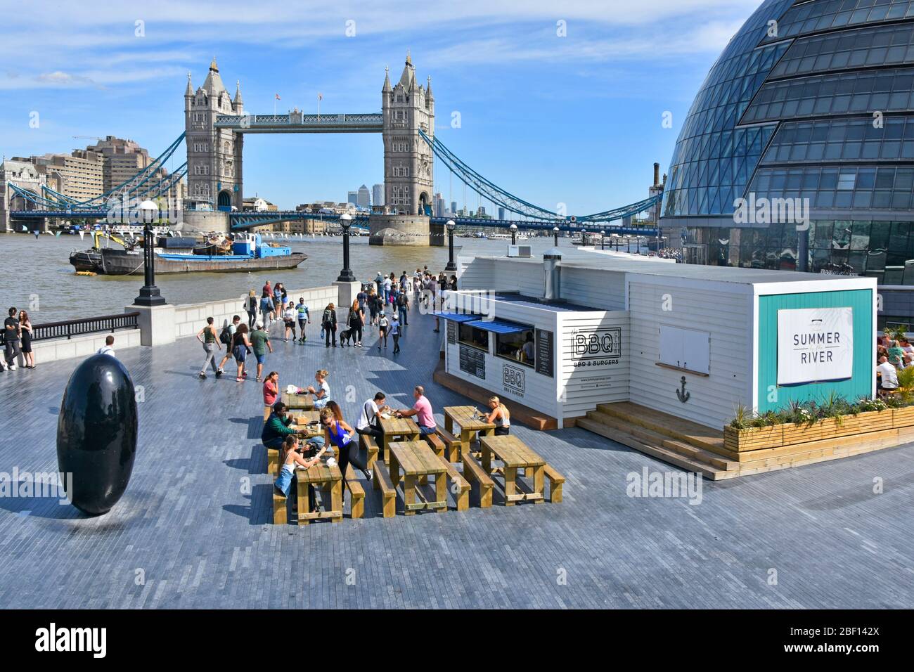 Tourists & office workers lunch time at fast street food stall riverside alfresco snacking at picnic tables River Thames & Tower Bridge Southwark UK Stock Photo