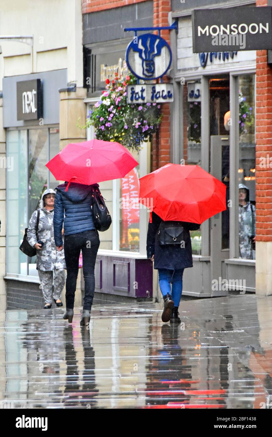 Raining two women walk in wet weather in town centre pedestrians only shoppers street zone in rain under red umbrella & reflections Durham England UK Stock Photo