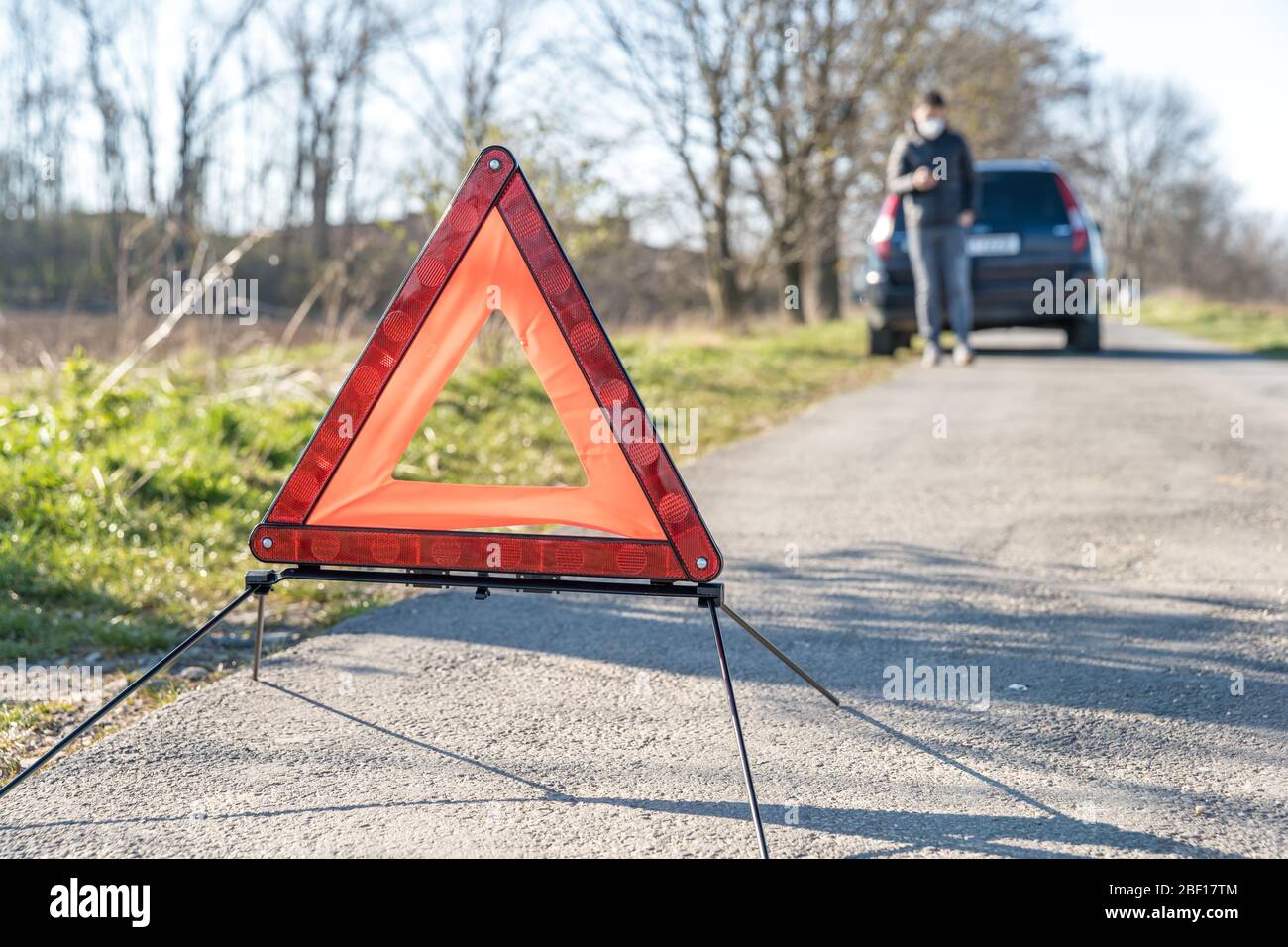 red warning triangle on the road in front of a broken car Stock Photo