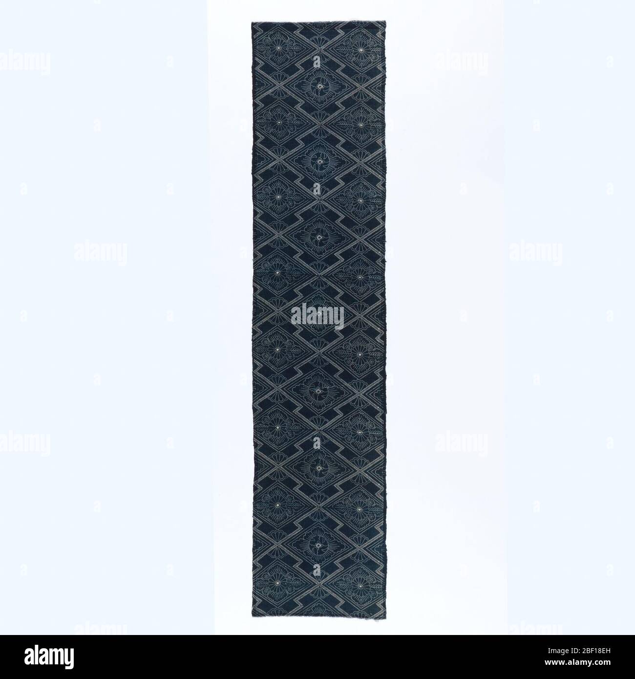 Textile. Length of stencil resist (katazome) with ivory pattern on blue ground. Zigzag lattice enclosing floral forms. Stock Photo