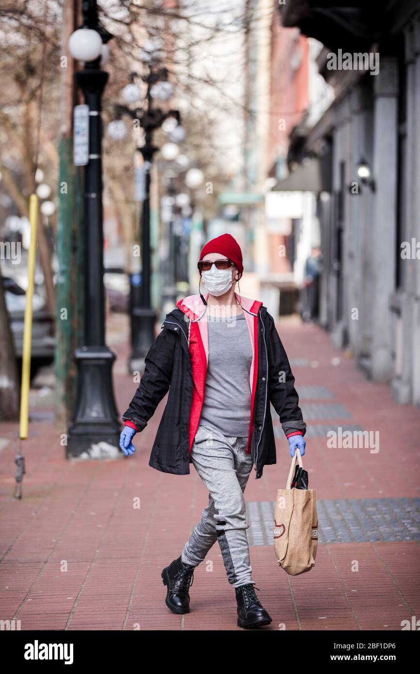 DOWNTOWN VANCOUVER, BC, CANADA - APR 01, 2020: Pedestrian in downtown Vancouver wearing a medical facemask and latex medical gloves for protetion from Stock Photo