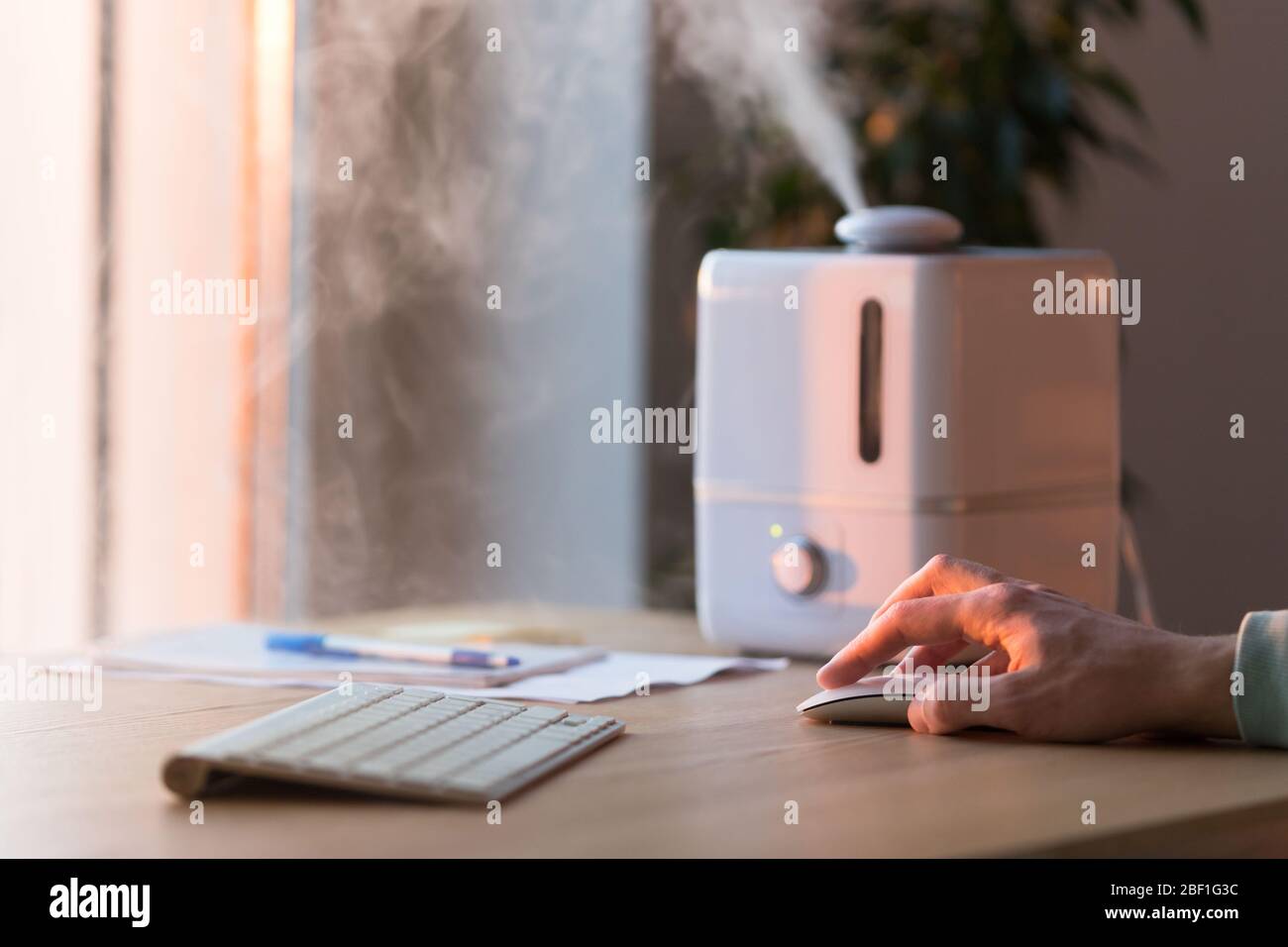 Man working on computer, using pc mouse near the aroma oil diffuser on the table, steam from humidifier, selective focus. Humidification of air in the Stock Photo