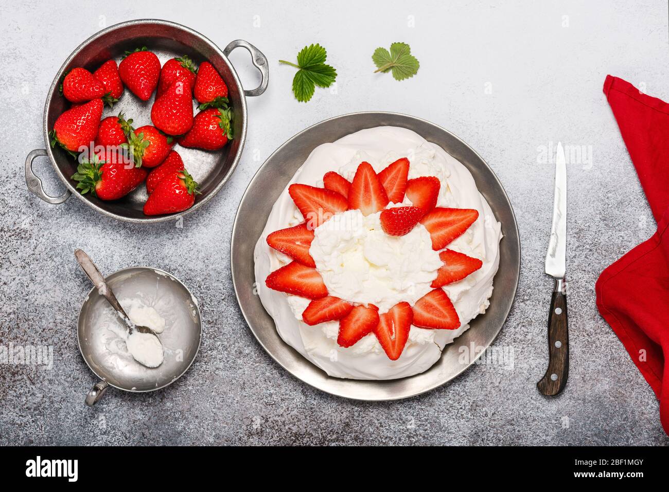 Adding some strawberries to whipped cream on meringue. Step by step recipe of Pavlova cake with strawberries. Top view. Copy space. Stock Photo