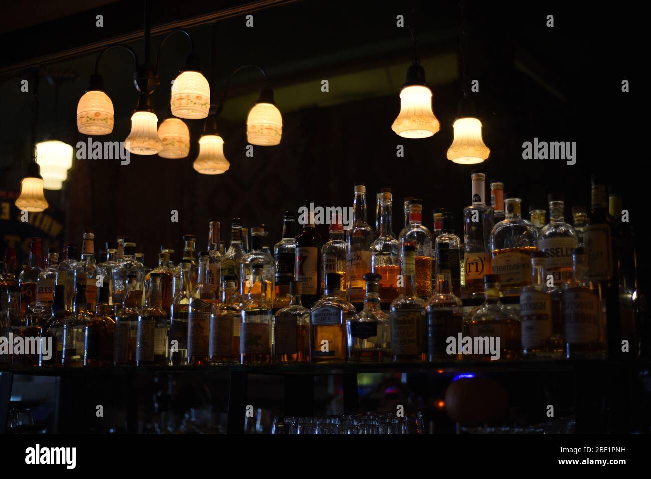 Overhead lights illuminate a variety of alcoholic spirits in bottles lining the wall in a bar Stock Photo