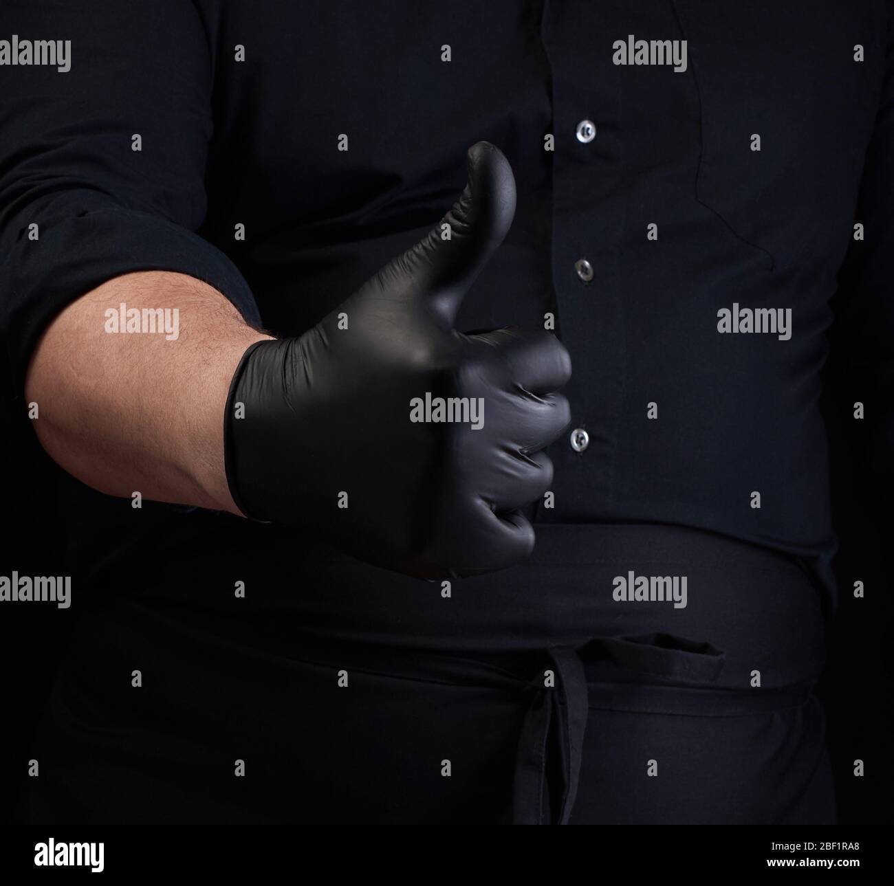 male cook in black uniform and black latex gloves shows like approval