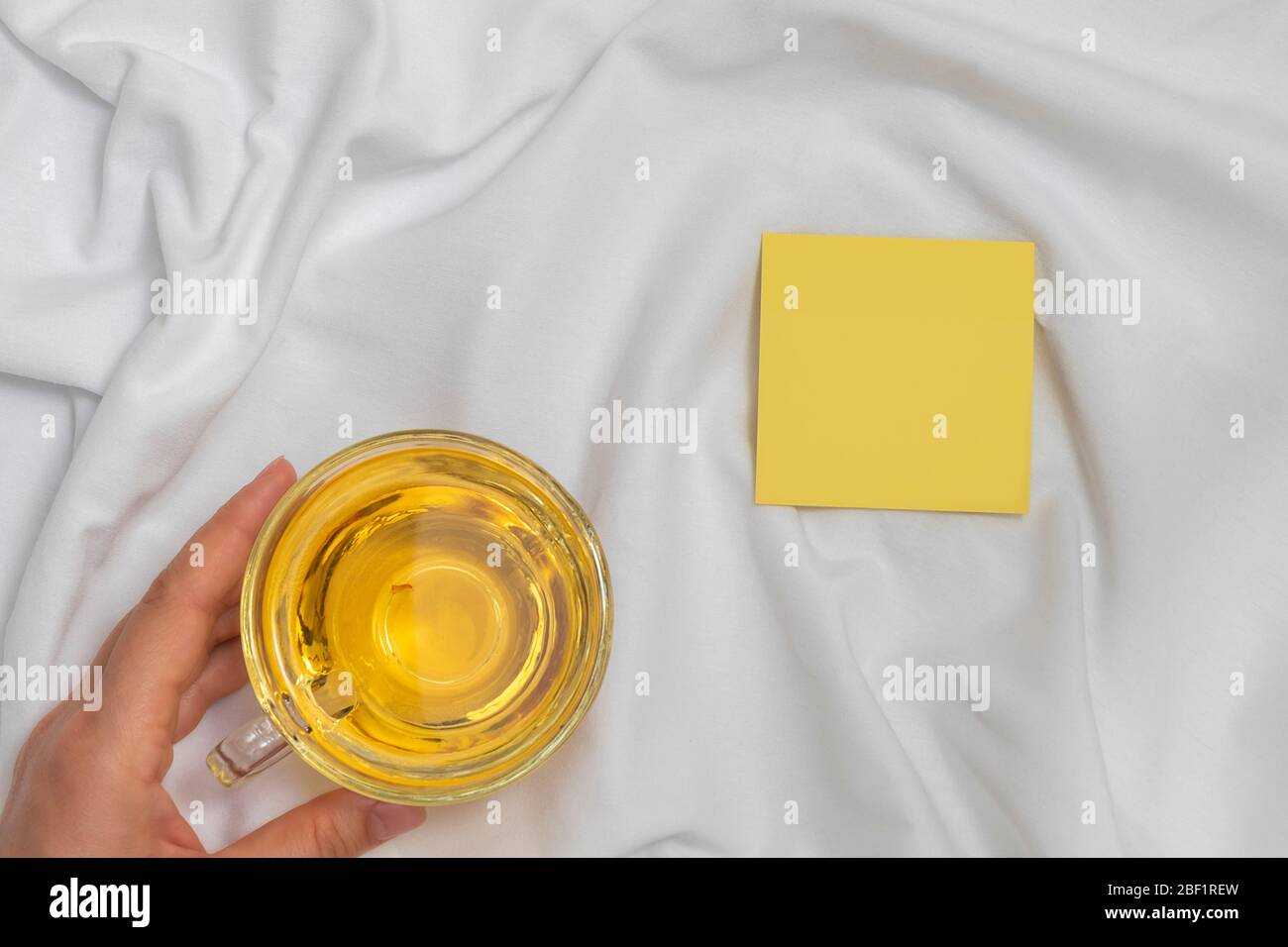 Woman hand holding cup of tea and empty sticky note on white bed ...