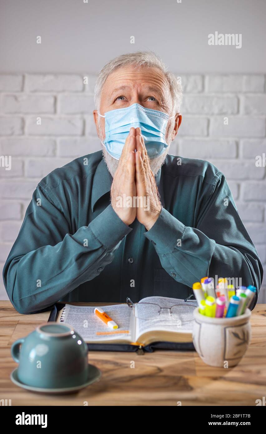 Man wearing medical mask on his face, before the Holy Bible and  a cup turned on his back, concept representing prayer and fasting for viruses protect Stock Photo