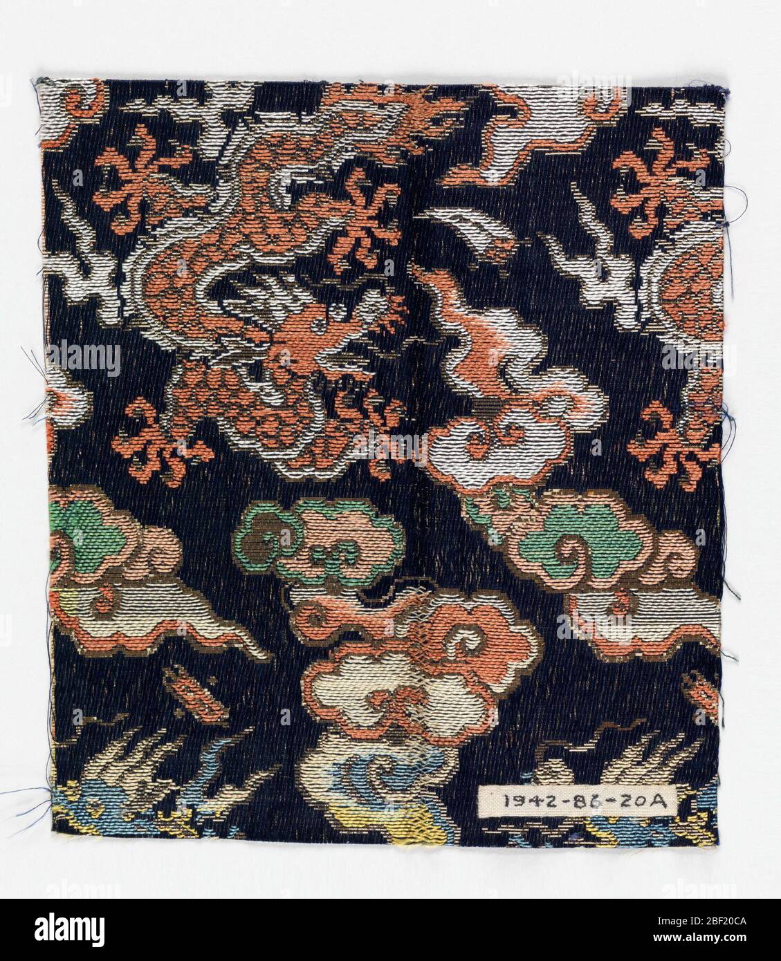 Textile fragments. Navy blue twill ground with woven supplementary weft pattern of large scale dragons and flying clouds in rust, white, yellow, green, and sky blue silk threads with metallic paper threads. Stock Photo