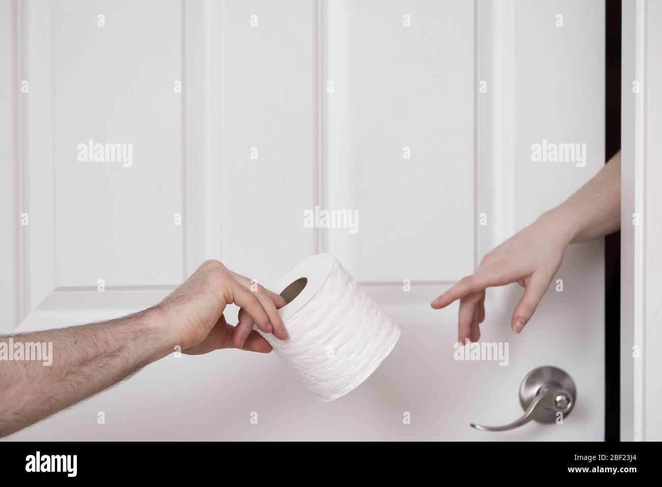 A mans hand passing a roll of toilet paper to a womans hand coming out of a door. Stock Photo