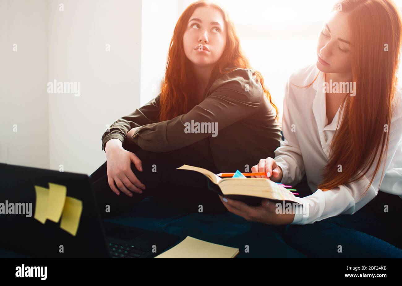 Two red-haired students study at home or in a student dormitory. they are preparinf for exams. One young woman is bored, and the second student is Stock Photo