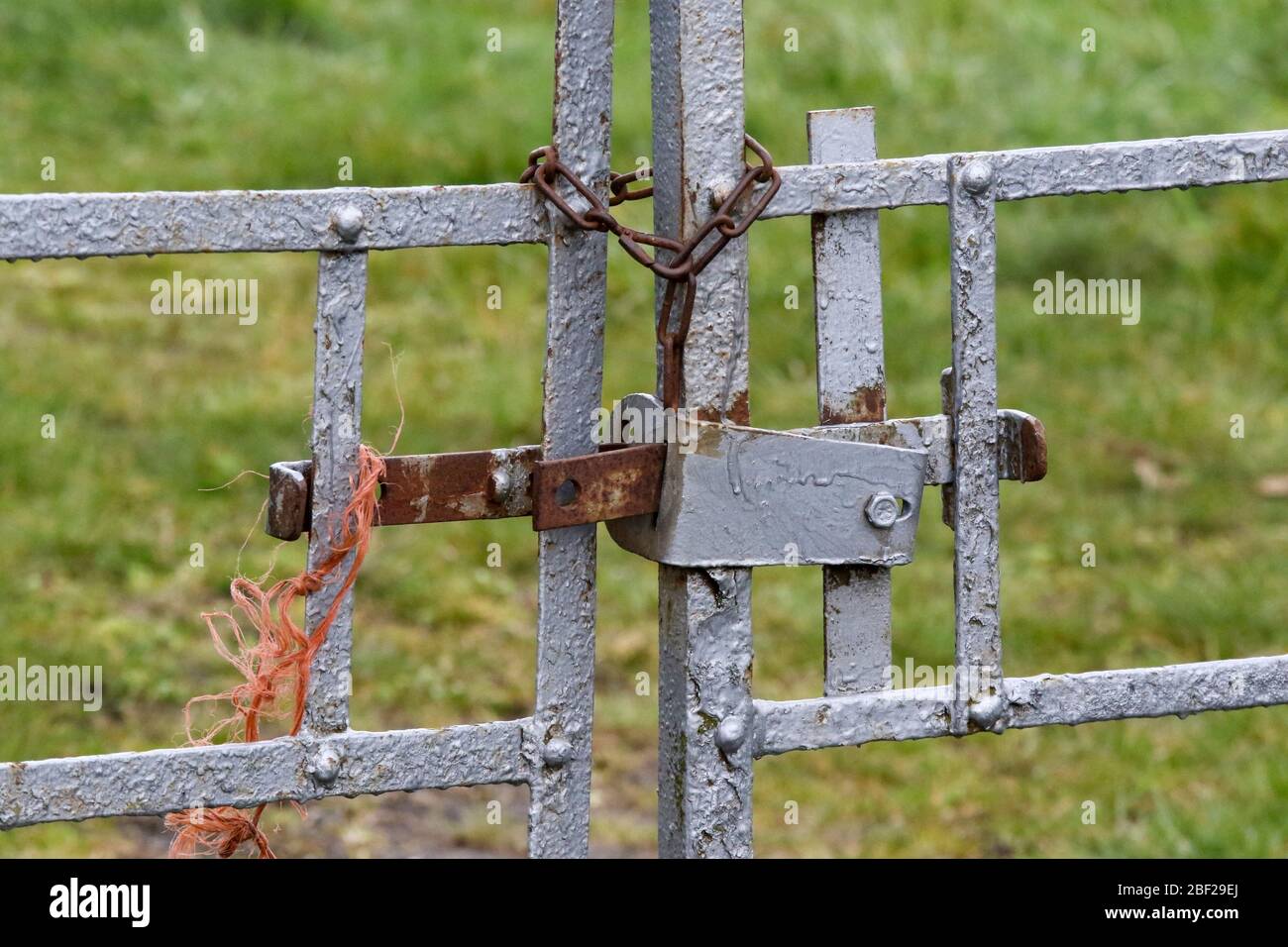 Old metal farm gates secured by cross-bar and orange nylon rope at entrance to field. Stock Photo