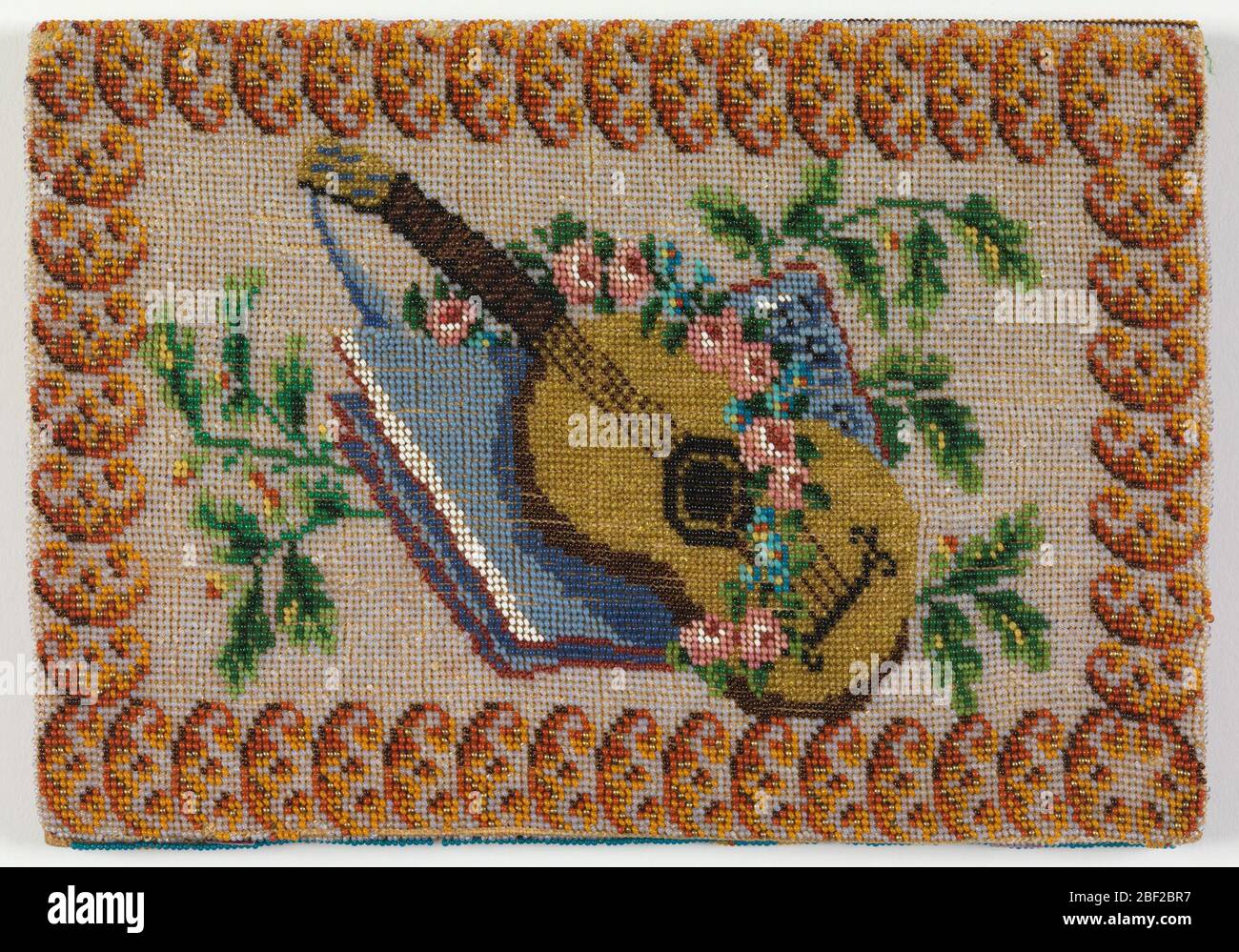 Notebook cover. Beaded fabric used to cover paper notebook. Image of a  guitar, book, bowl and flowers on a white ground with a border on one side  and a leaf pattern in