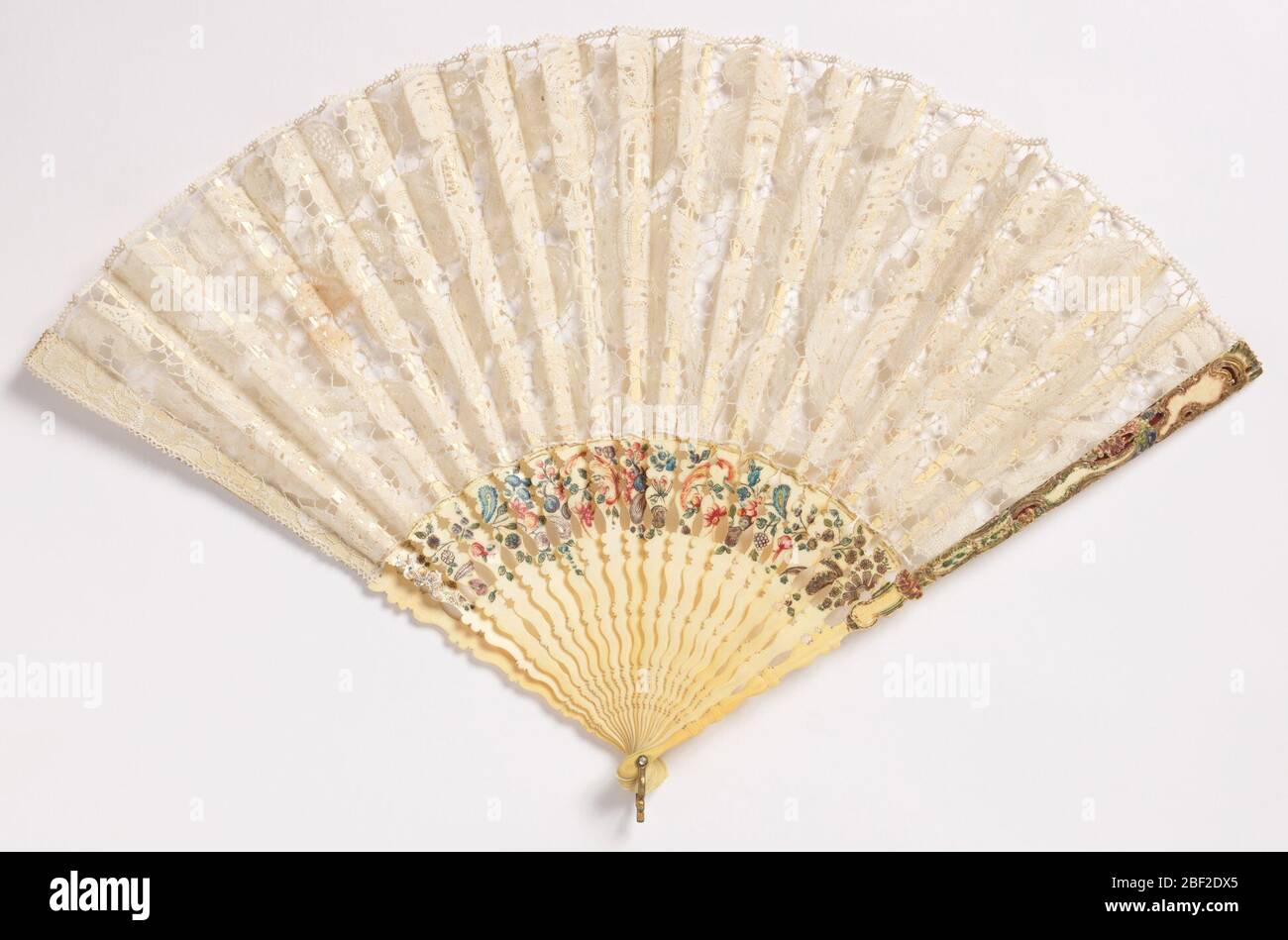Pleated fan. Pleated fan. Leaf of 17th century white Milanese bobbin lace. Carved and painted ivory sticks with flowers and feathers. Guards carved with baroque detail and painted. Rivet is set with faceted glass. Gilt metal bail. Stock Photo