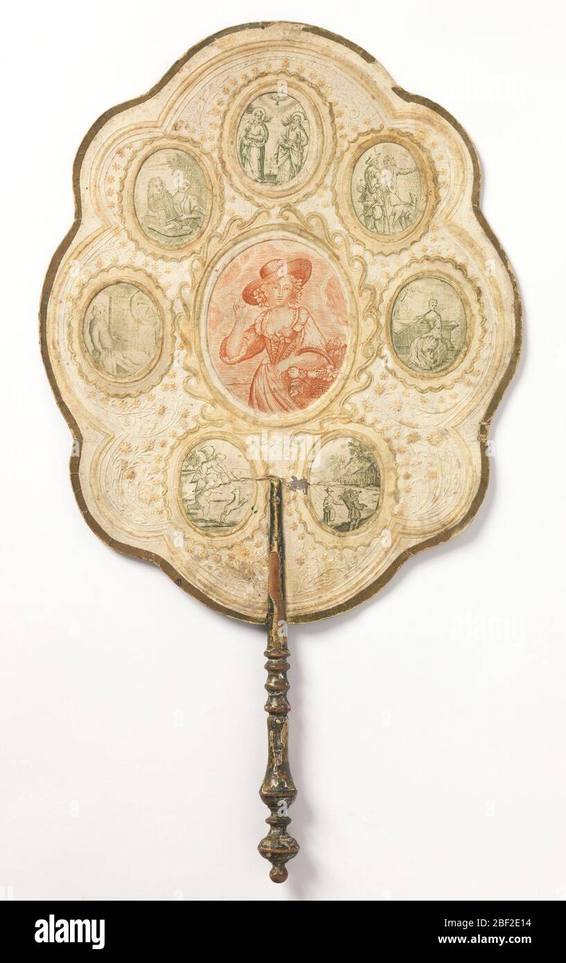 Handscreen. Shaped leaf of paper with embossed scrolls and flowers, gold edges, and a turned wood handle. On each side there is a larger center medallion printed in red, surrounded by seven smaller medallions printed in green. Stock Photo
