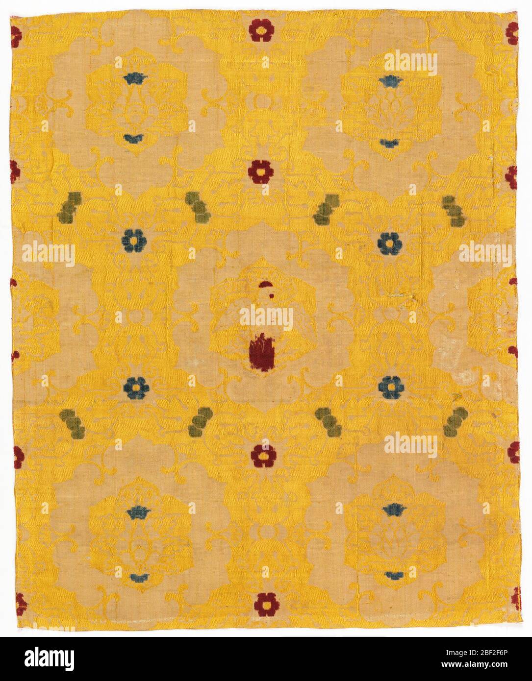 Textile. Heavy symmetrical leafy ogee-type grid framing blossoms in 6-lobed medallions in white on a yellow background. The medallion in the center of the fabric holds a phoenix rising from a pyre bearing a scroll 'NORS VIVE' in mirror imaged letters. Stock Photo