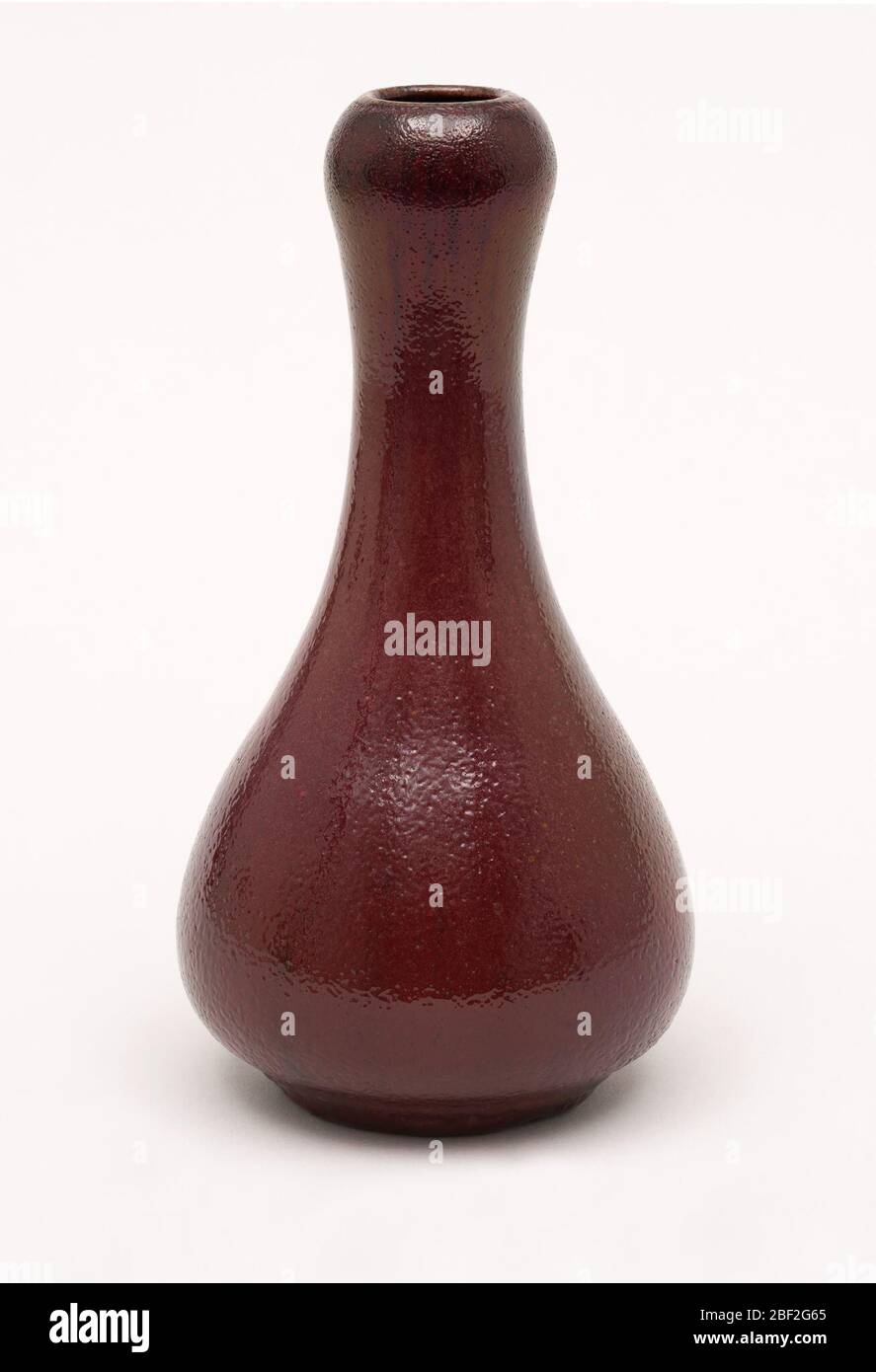 Vase. Gray-white stoneware body, thrown. Bulbous body with tapering neck; with slightly bulging area below rim; flat foot. Covered with a deep red or scarlet glaze with slight golden luster effect. Black striations through glaze. Very dark red at rim bulge. Stock Photo