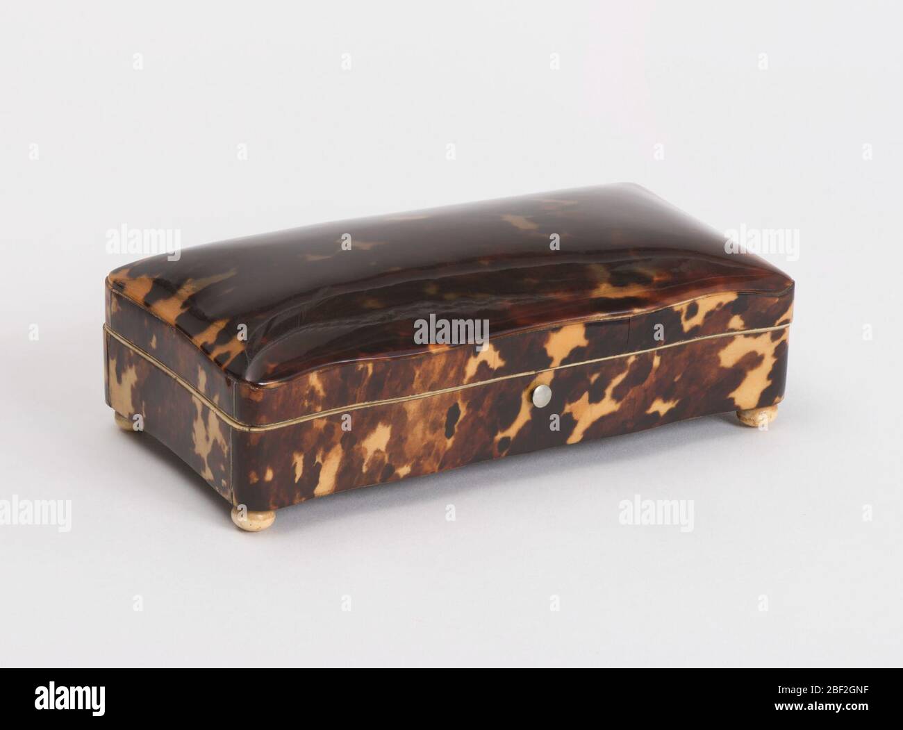 Box. Rectangular box of wood with wavy sides and hinged cover. Sides covered with flamy tortoise-shell; top cover is domed sheet of tortoise-shell without backing. Inside edges lined with strips of ivory, the box itself with dark purple velvet. Stock Photo