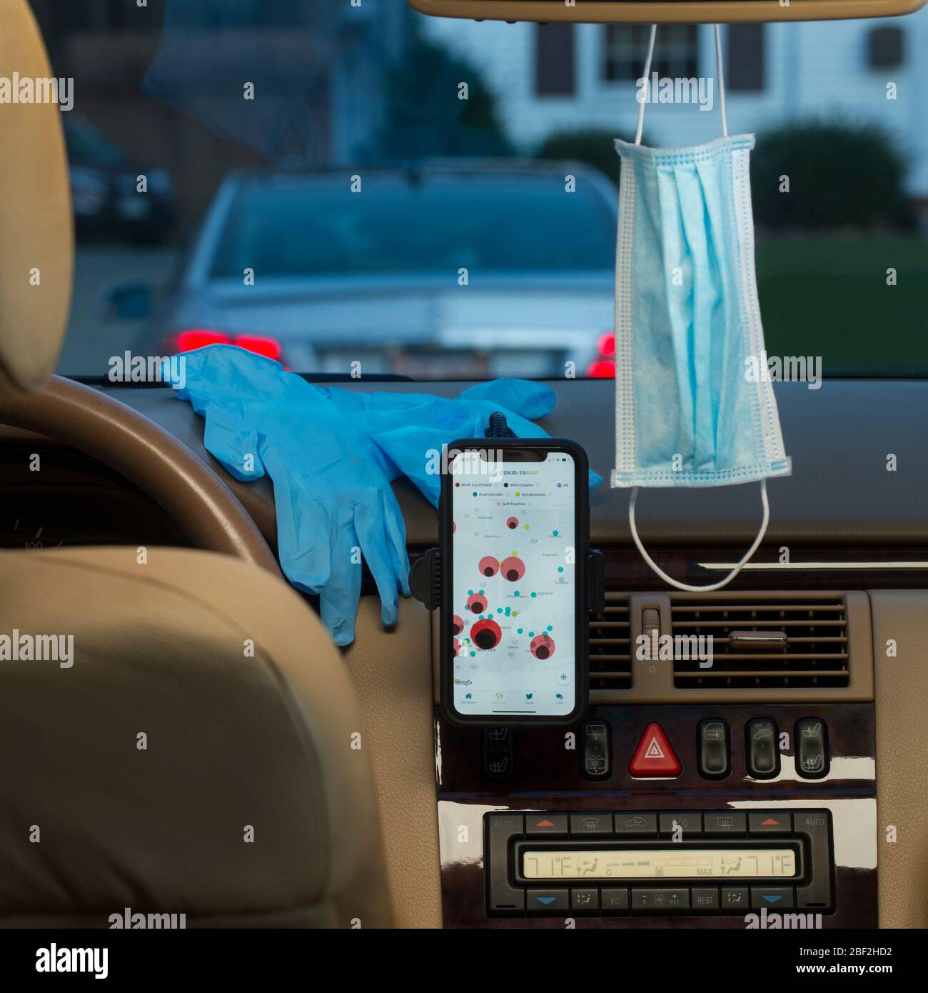 COVID-19: iPhone 11 displaying HealthLynked COVID-19 Tracker, face mask and latex gloves on the dashboard of a vehicle. Stock Photo