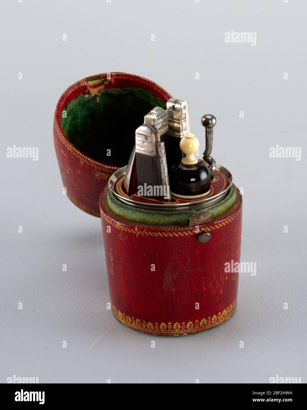Case. Barrel-shaped red leather case with stamped gold decoration along the borders (bottom, centre, top). Case opens in the centre, small press button on front, hinge on back. Inside covered in green velvet. Small press-button on the front, hinge on back. Stock Photo