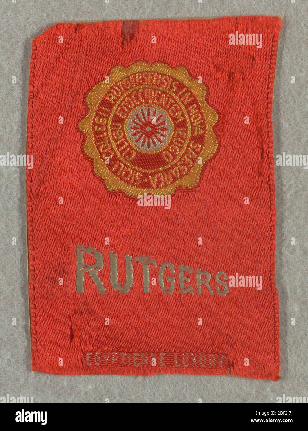 Souvenir. Red tobacco silk from Egyptienne Luxury cigarettes with seal of Rutgers University in yellow and white. Just below is 'Rutgers' in white sloping capital letters. Stock Photo