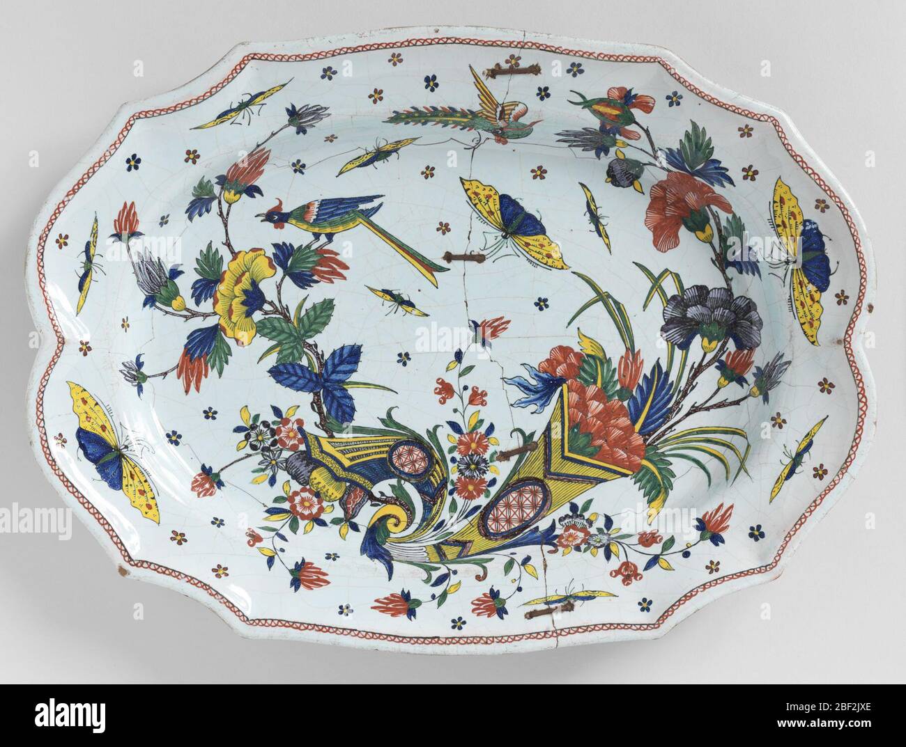 Platter. Irregular scalloped border, oval cavetto. Decoration in Chinese style. Double cornucopia with flowers, large insects and a long-tailed bird Stock Photo