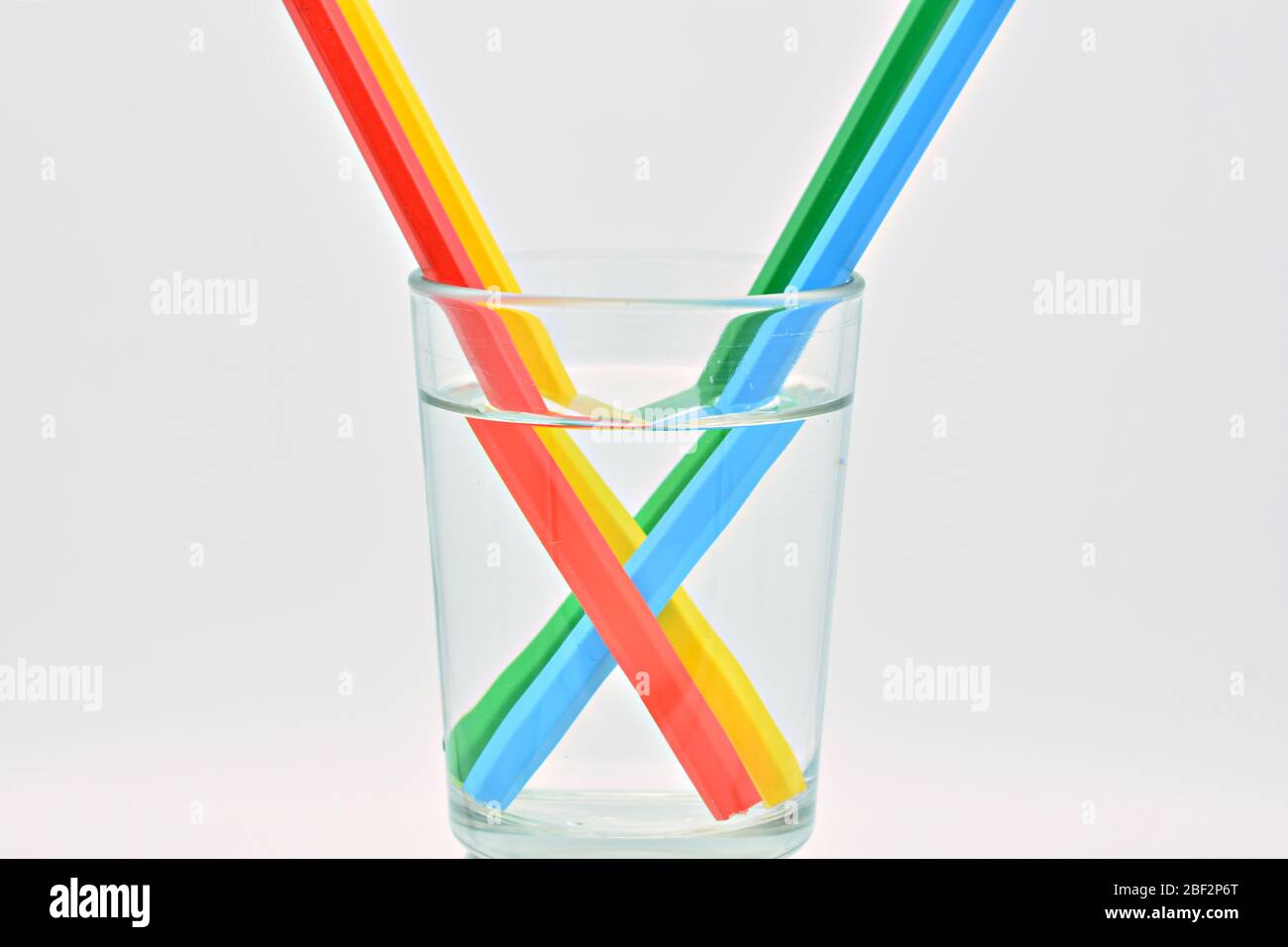 Blue, yellow, green and red colored pencils, inside a glass filled with water, explanation refraction of light Stock Photo