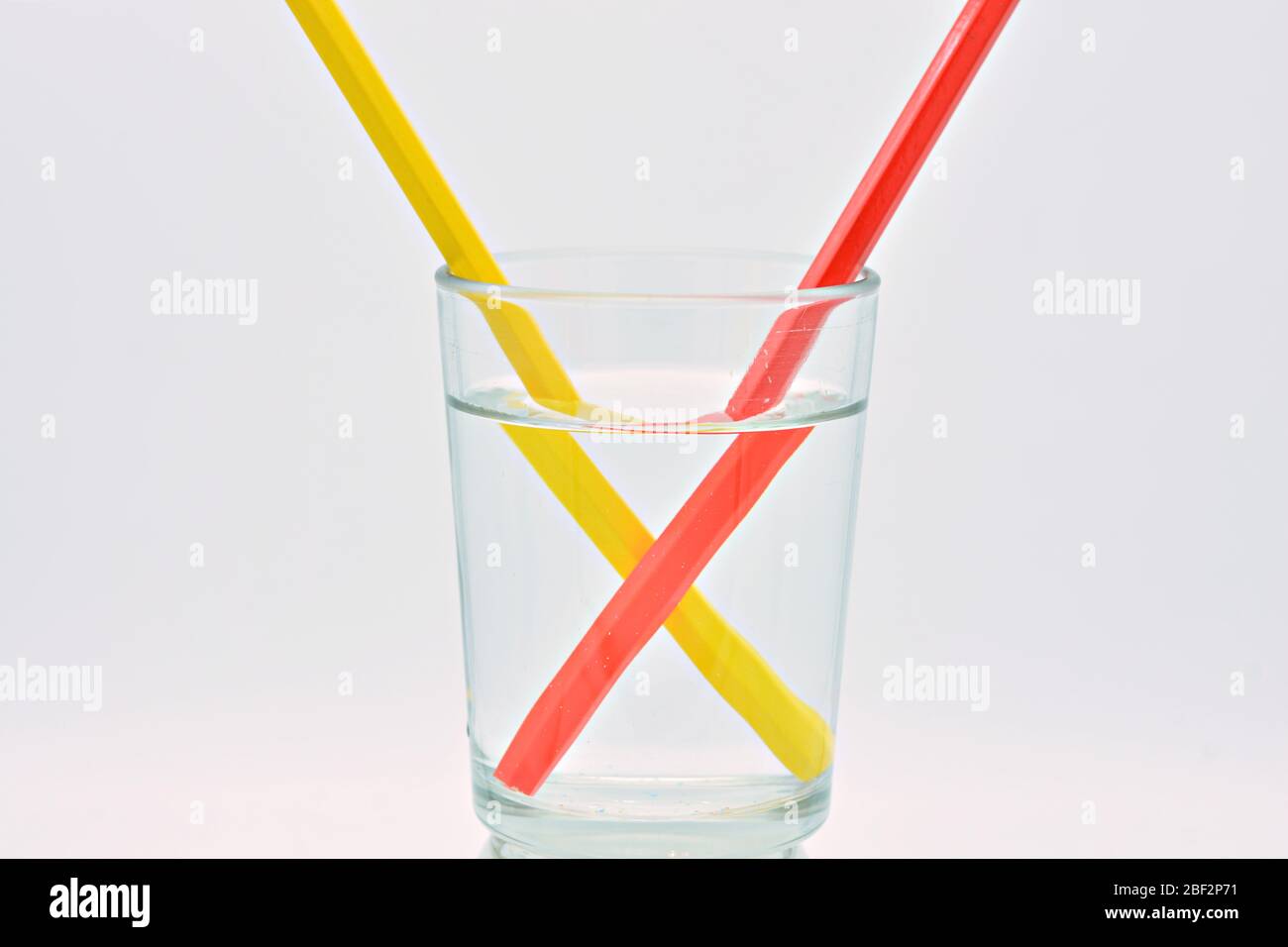 Yellow and red pencils, inside a glass filled with water, light refraction explanation Stock Photo