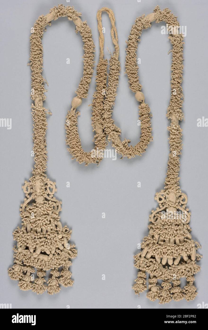 Cord with tassels. A long cord completely covered with knotting and braiding, to which are attached two equally large tassels arranged in tiers of elaborate knotting and braiding. Stock Photo