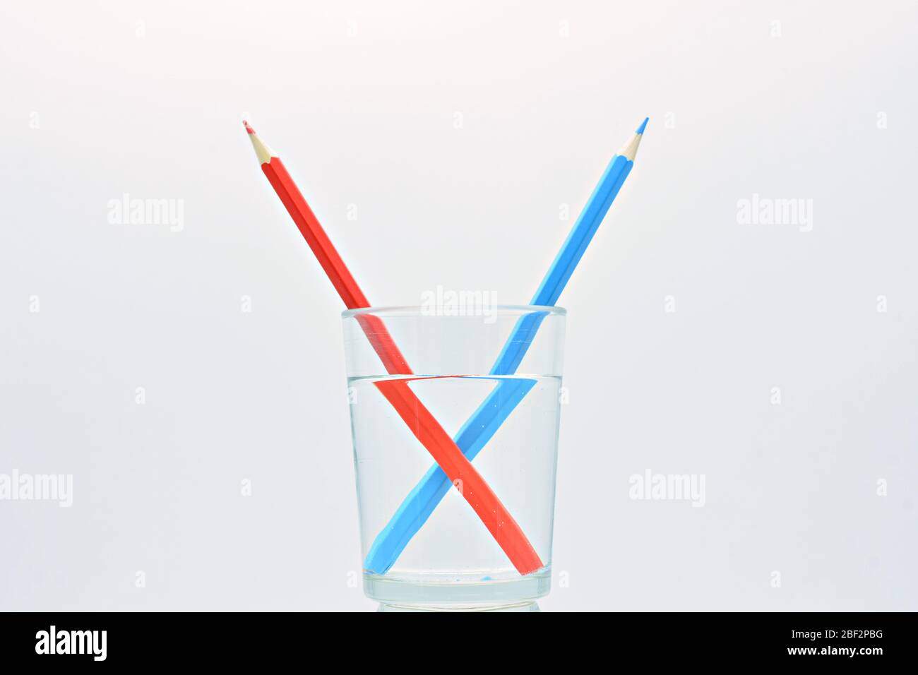 Blue and red colored pencils, inside a glass of water, explanation refraction of light Stock Photo