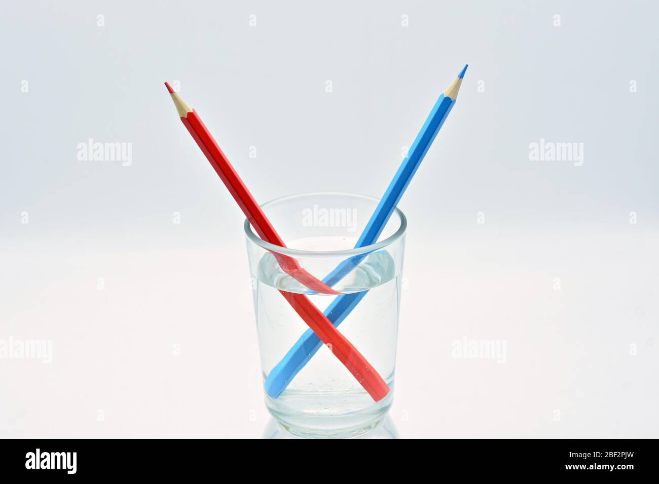 Blue and red colored pencils, inside a glass of water, explanation refraction of light Stock Photo