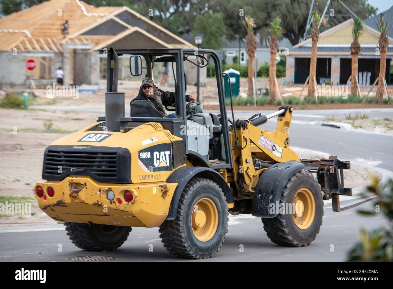 Tractor driver moving equipment where needed for new home construction development in central Florida during coronavirus stay at home order Stock Photo
