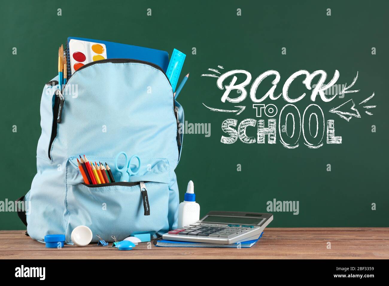 Backpack and stationery on table near blackboard with phrase BACK TO SCHOOL Stock Photo
