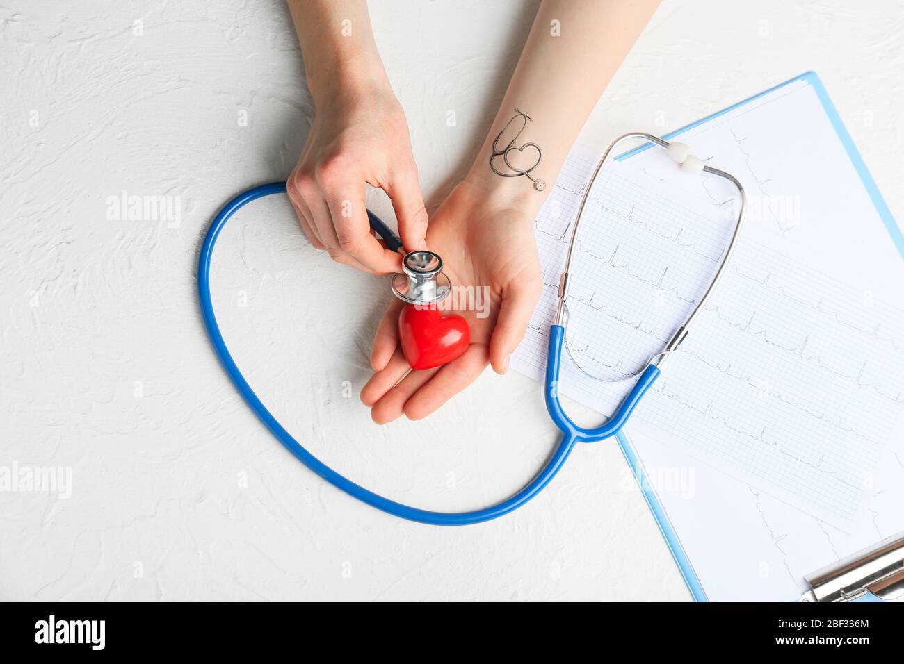 Hands of cardiologist with stethoscope, heart and cardiograms on white ...