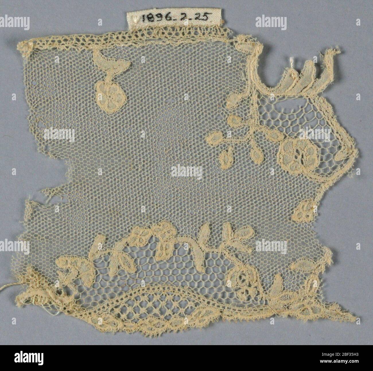 Fragment. Brussels-style fragment showing reserve area on the border filled with bobbin imitation of needlepoint openwork stitches and set off by tiny floral wreath. Vrai droschel ground. Stock Photo