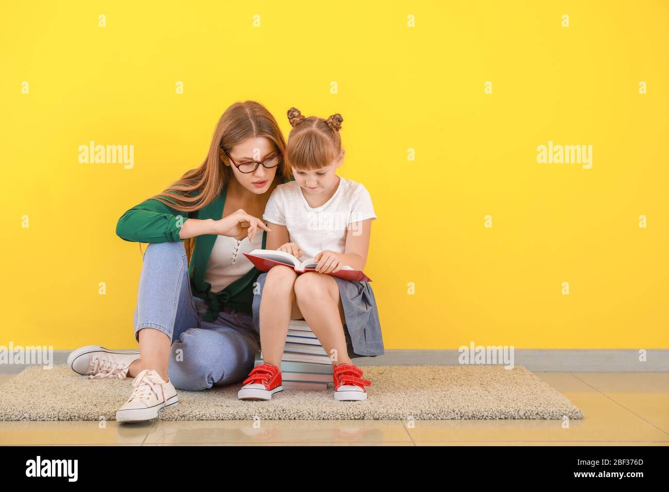 Cute little girl and her mother reading books near color wall Stock