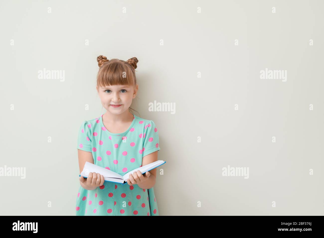Cute little girl with book on light background Stock Photo - Alamy
