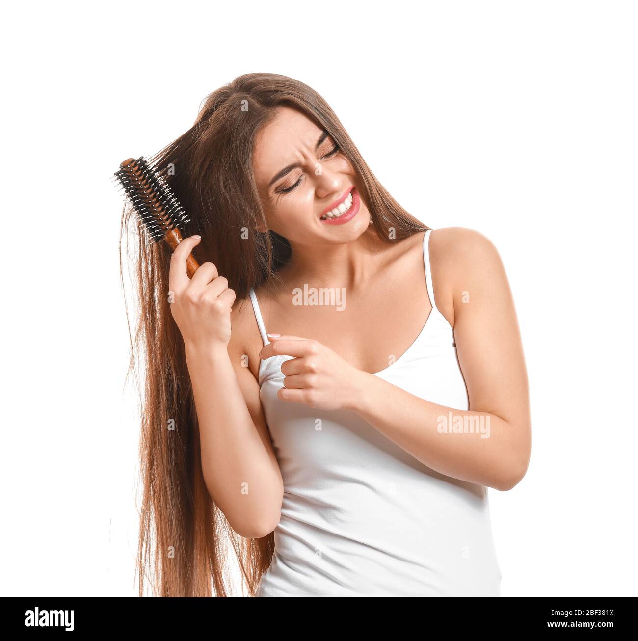 Stressed woman trying to brush tangled hair against white background